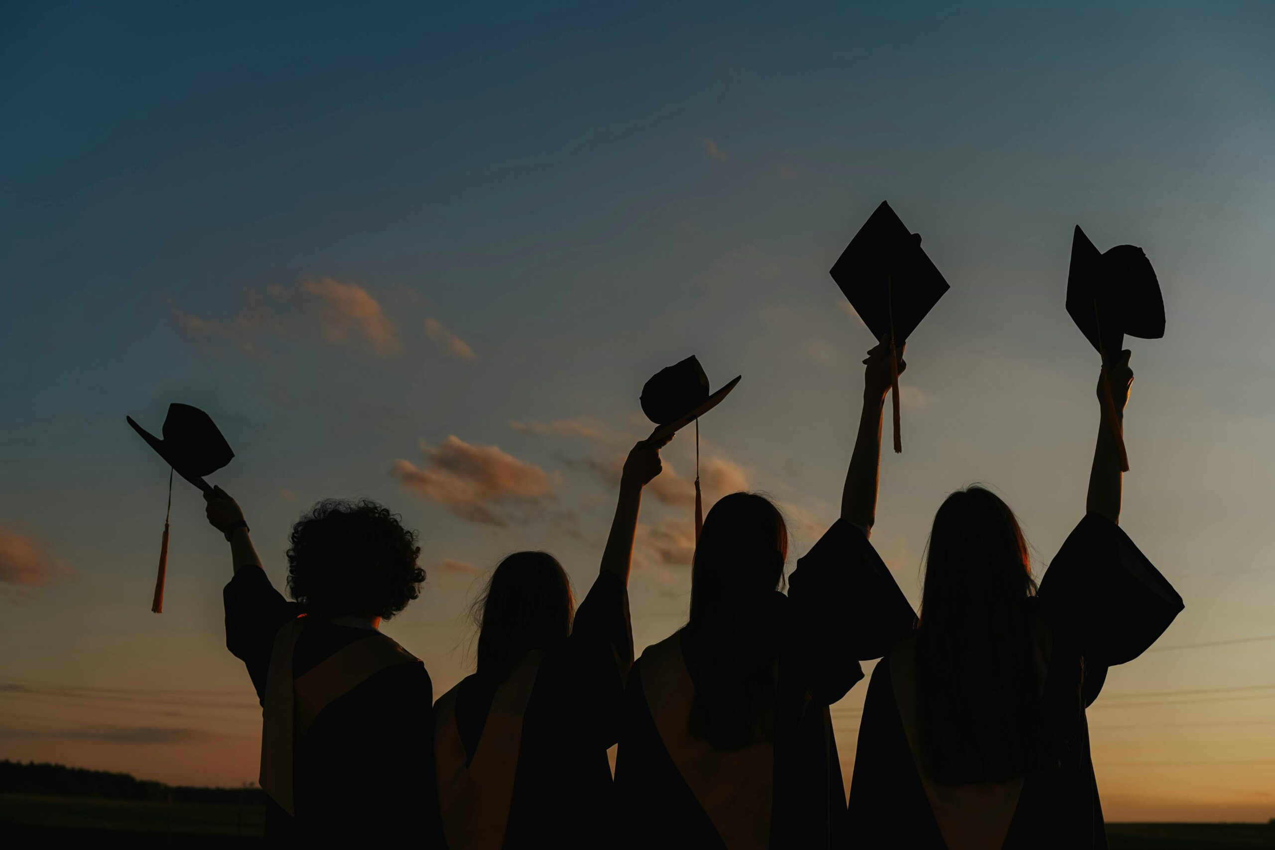 Silhouette of graduates raising caps in joy at sunset.